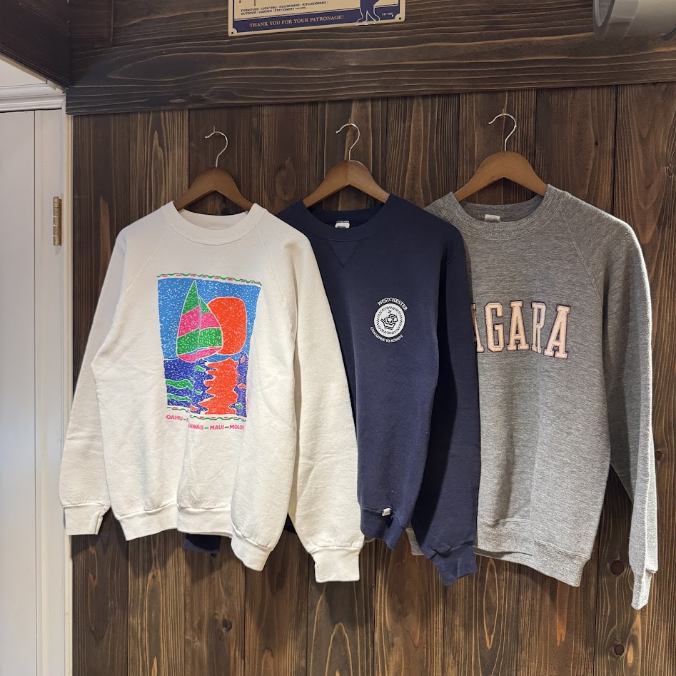 80年代アメリカ製スウェット特集—グレー・ネイビー・ホワイトの3枚を木壁にハンガー掛けで並べたキービジュアル