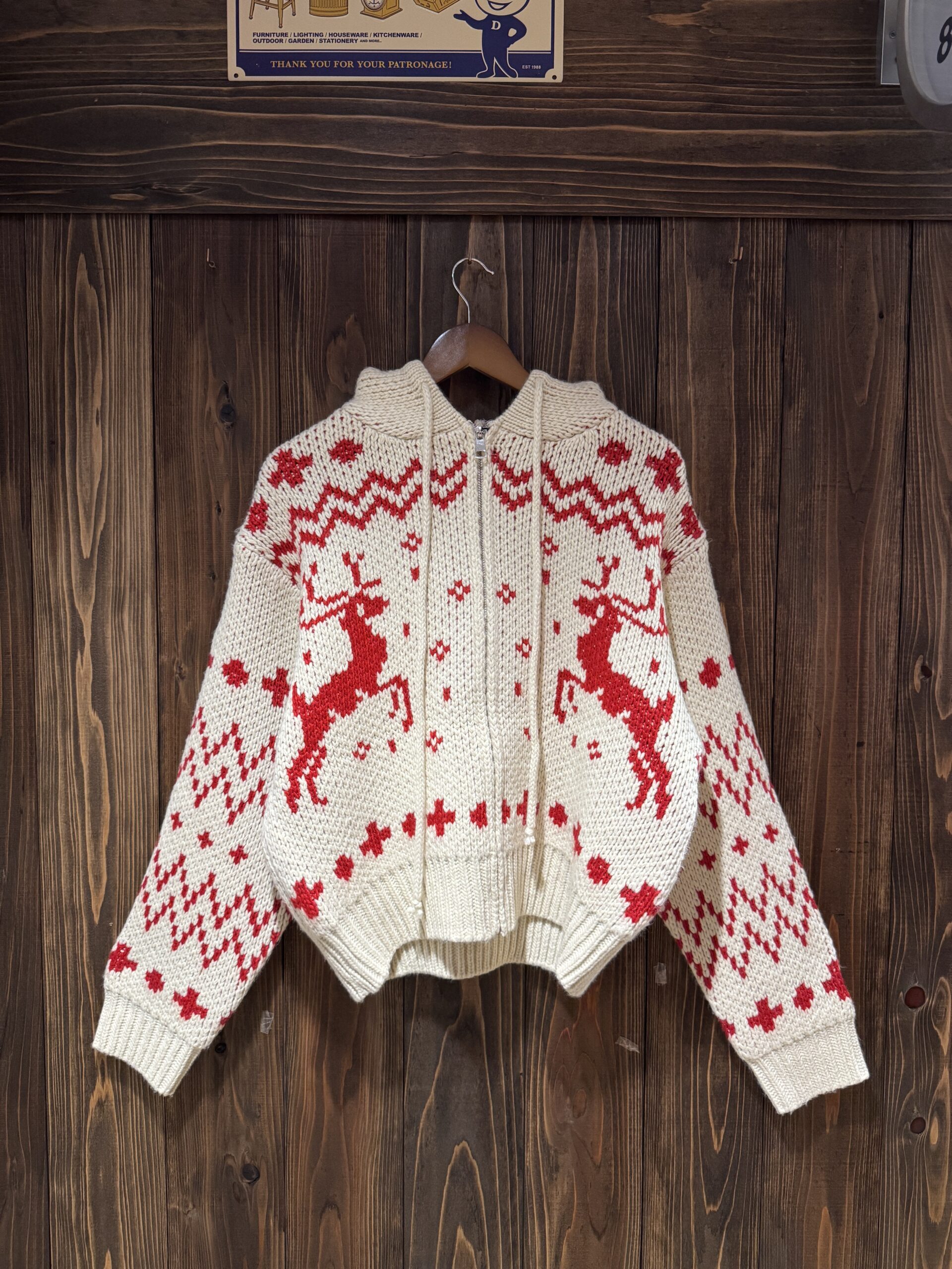 木の壁に掛けられた、and more（韓国・ソウル）のトナカイ柄フルジップニットパーカー前面。