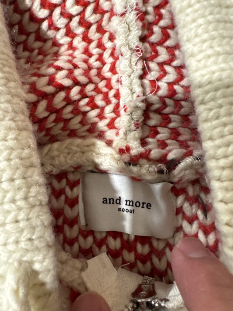 and more seoul のブランドタグのアップ。クリームと赤のローゲージ編み目が裏側から見える。
