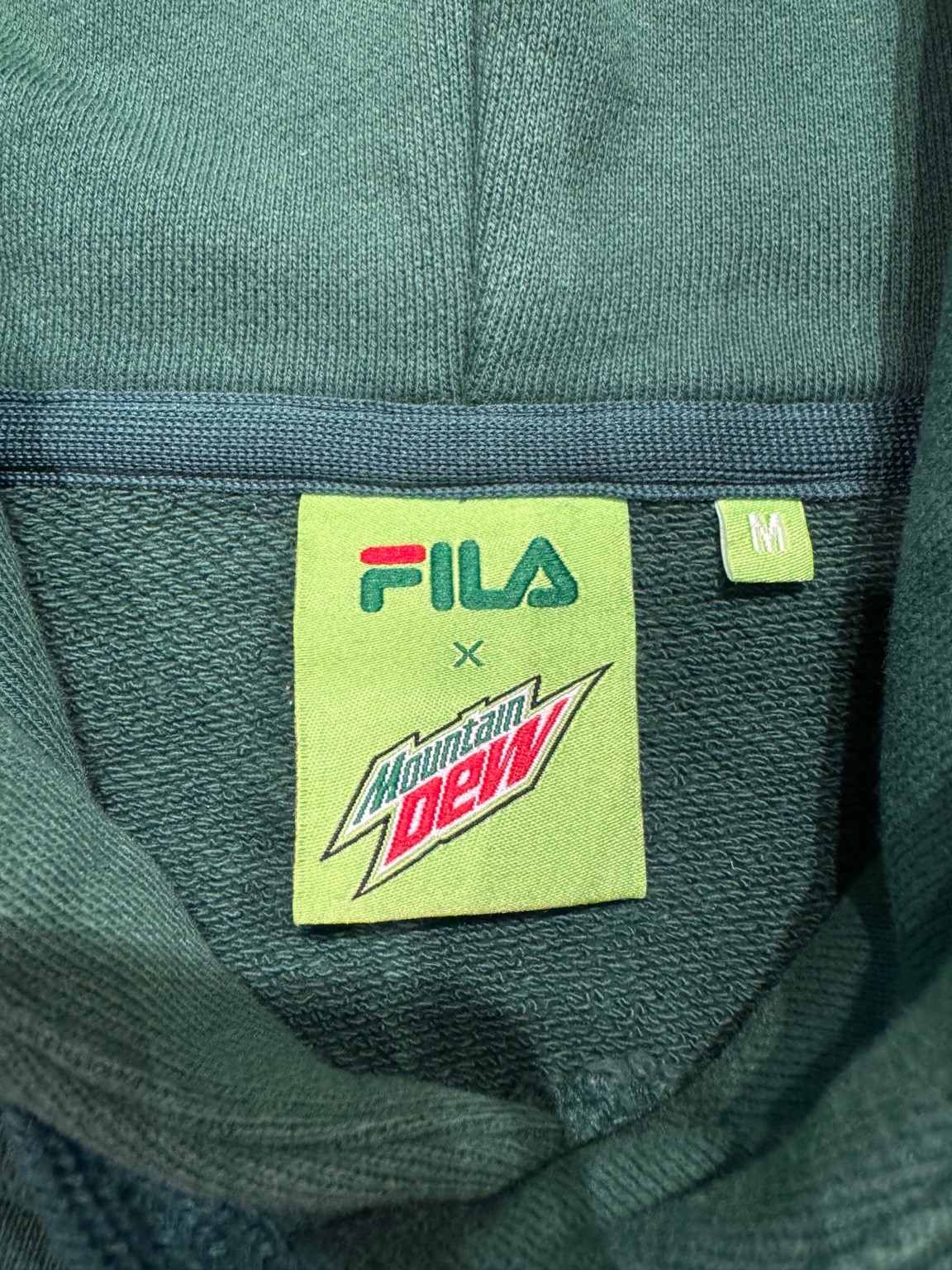 FILA × Mountain Dewフーディの首元に付いたコラボタグのクローズアップ写真。