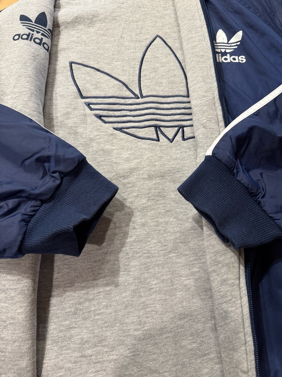 ネイビーナイロン面とグレースウェット面が重なるように写ったディテール写真。両面にトレフォイルロゴが入っている。