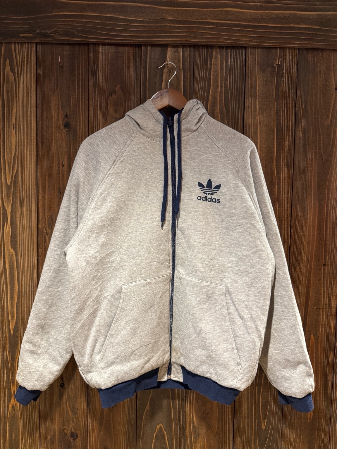 グレーのスウェット面を表にしたアディダスリバーシブルフーディのフロント全体。胸にネイビーのトレフォイルロゴプリント入り。