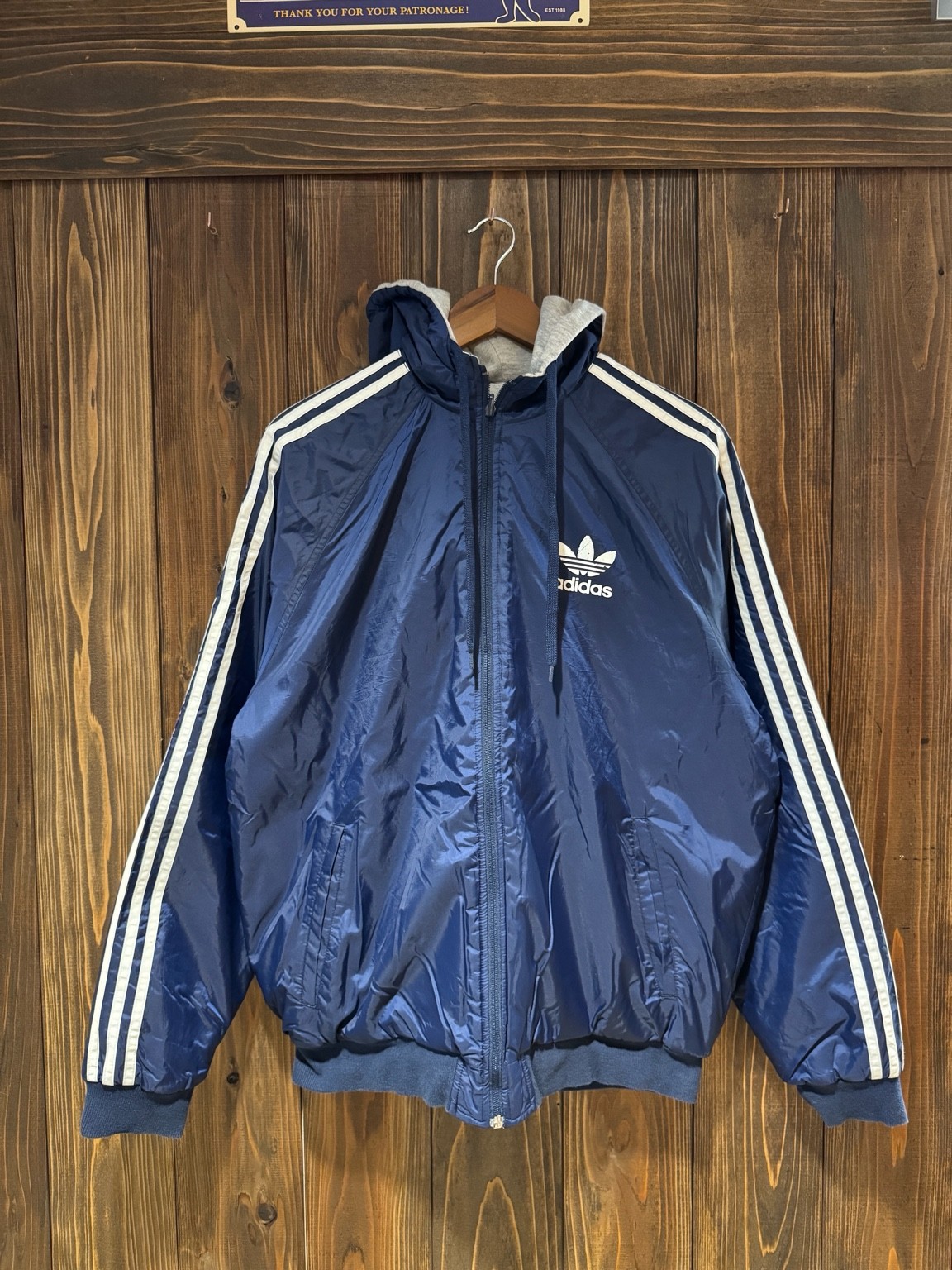ネイビーのナイロン面を表にしたアディダスのリバーシブルフーディ。胸にトレフォイルロゴ、袖に3本線が入ったフロント全体。