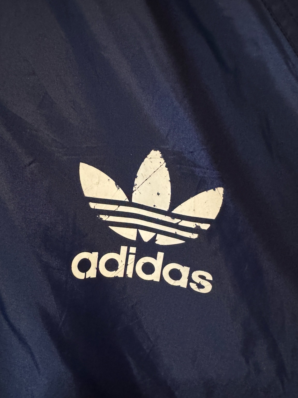 ネイビーナイロン面の胸に入ったトレフォイルロゴプリントのアップ。ひび割れがあり、古着らしい雰囲気になっている。