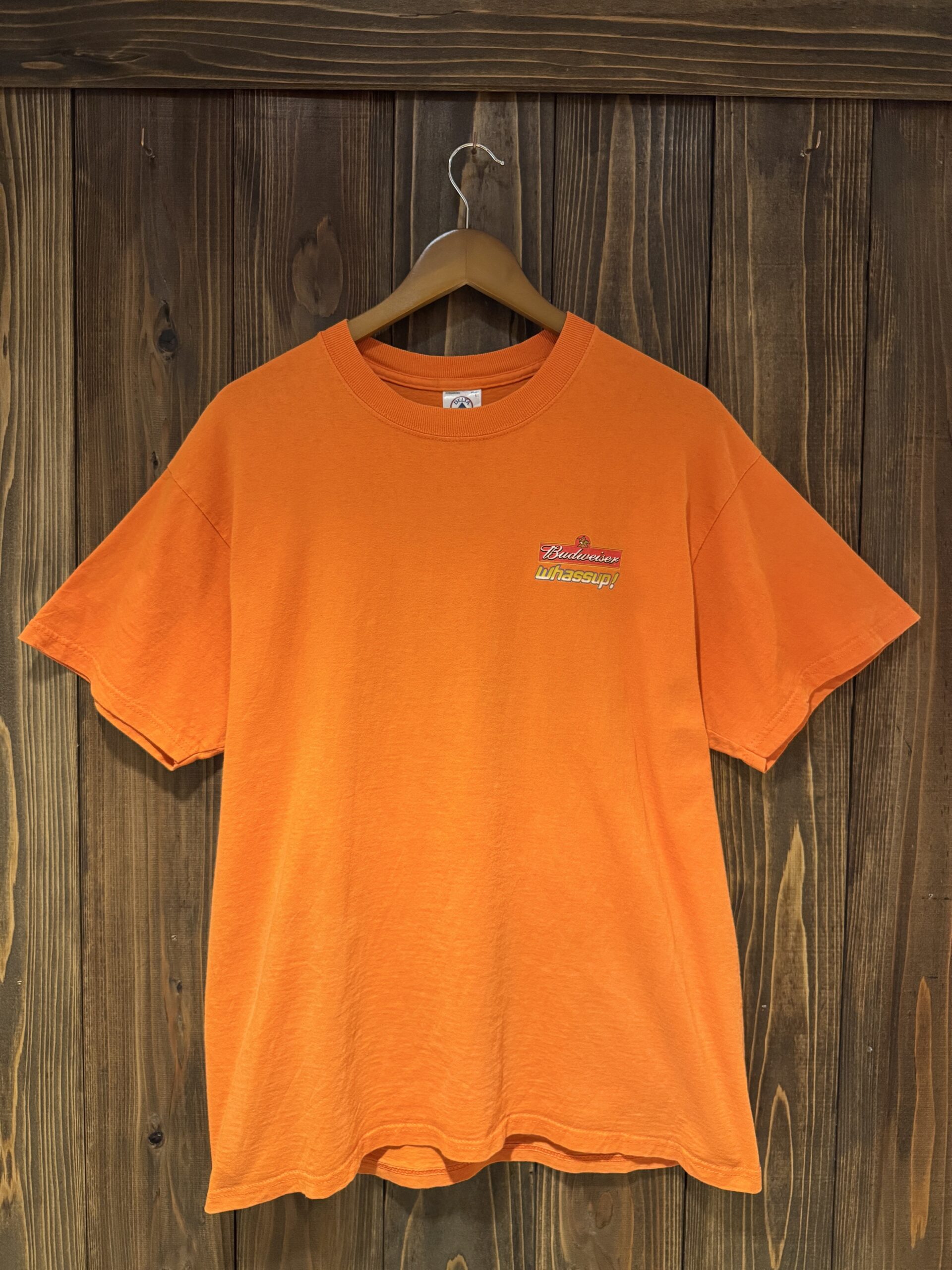 オレンジボディのBudweiser企業物Tシャツ。胸元に小さく「Budweiser whassup!」ロゴが入ったフロントハンガーショット。