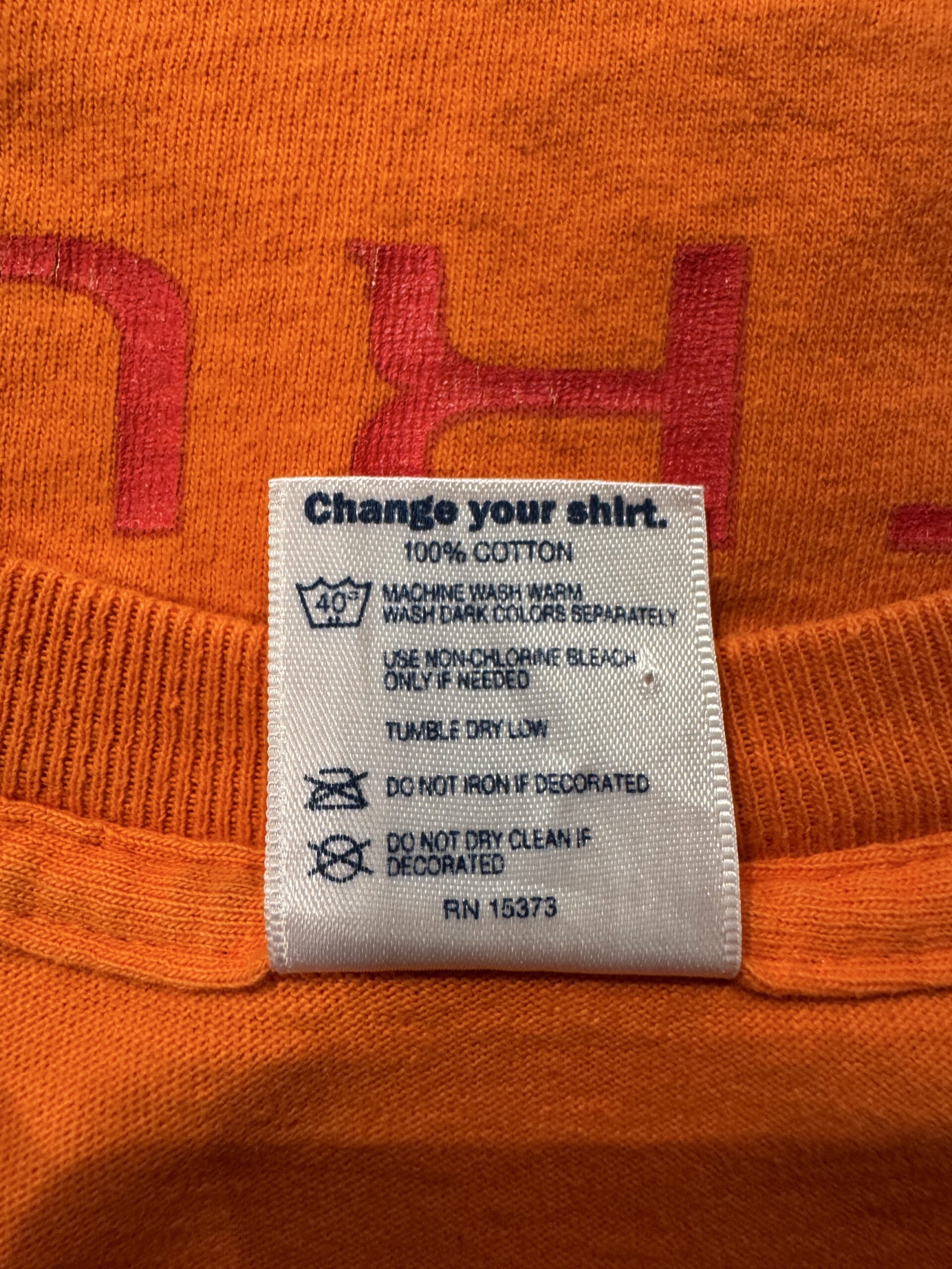 Change your shirt. のメッセージと、100% COTTON・洗濯表示が記載されたケアタグのアップ写真。