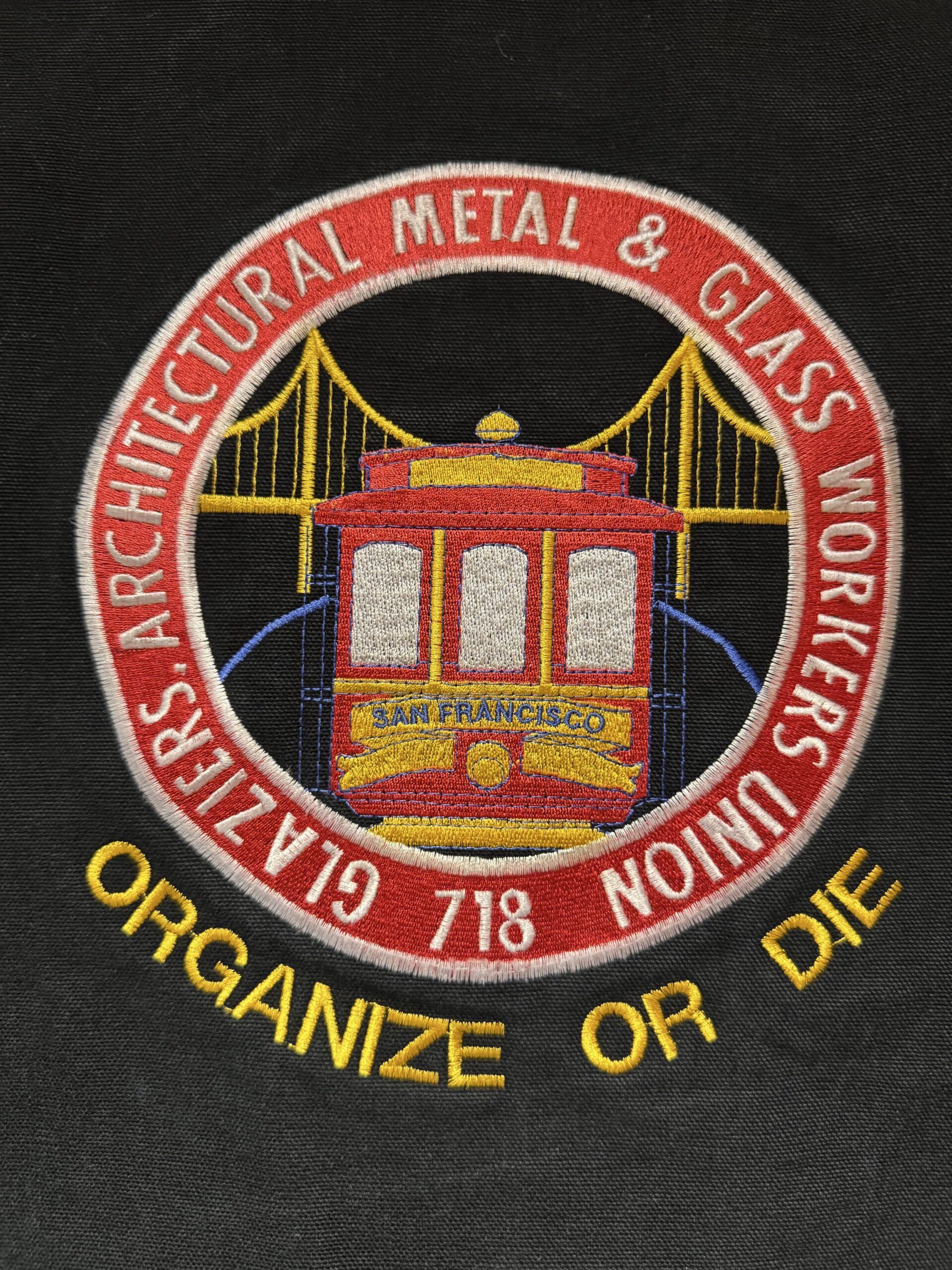 ARCHITECTURAL METAL & GLASS WORKERS UNIONのバックワッペン刺繍アップ。ORGANIZE OR DIEのメッセージが入っている。