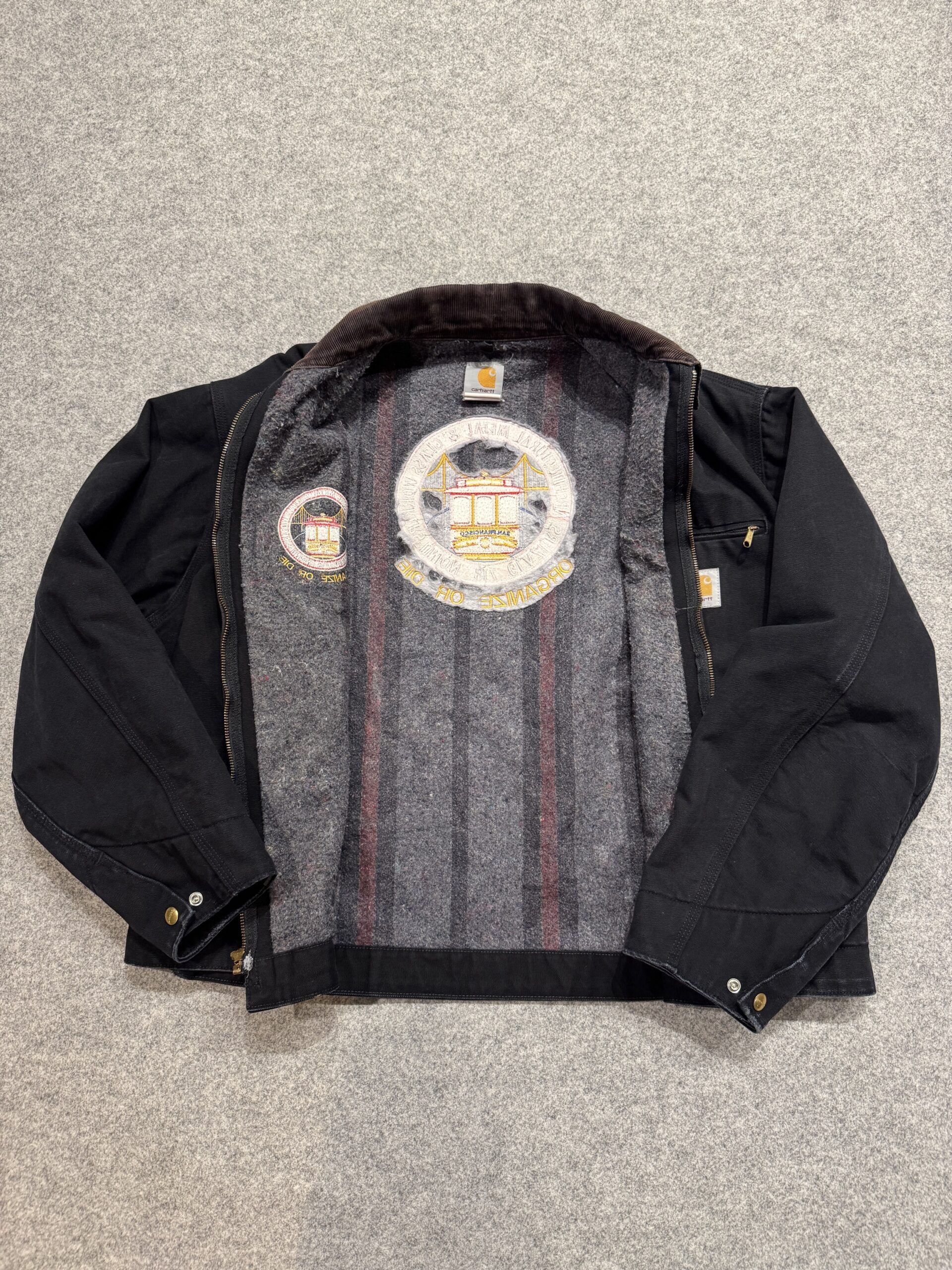 床に広げた状態のCarharttワークジャケット。全面に入ったブランケットライニングと大きなワッペン裏が見える。
