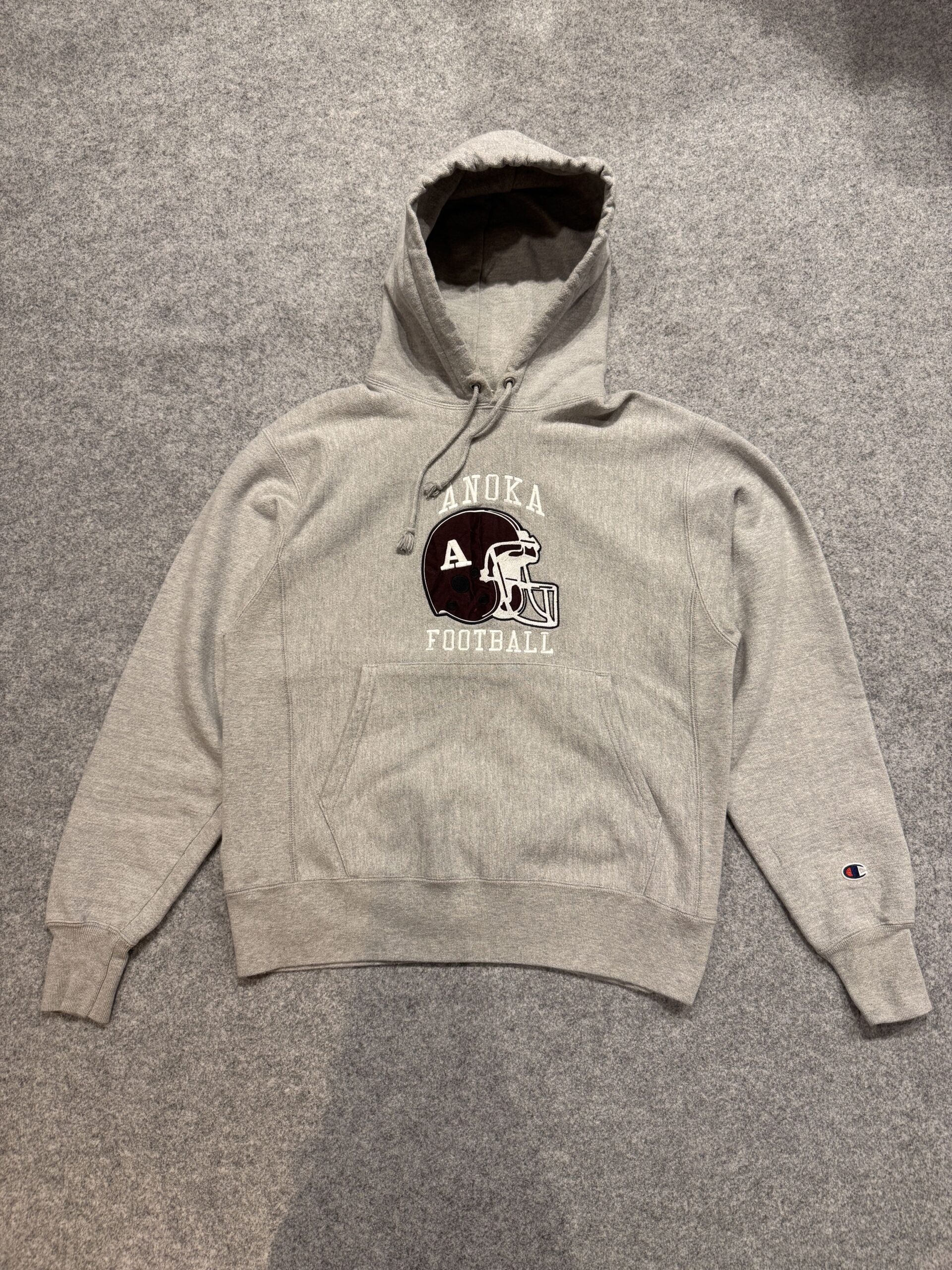 ChampionリバースウィーブのANOKA FOOTBALLフーディーを床に平置きしたフロント全体画像。