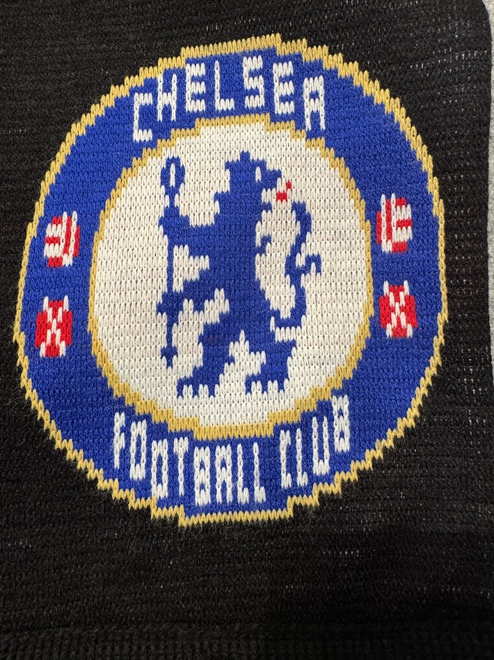 チェルシーFCのエンブレム部分の編み柄アップ。青い円形の中にライオンが描かれたデザイン。