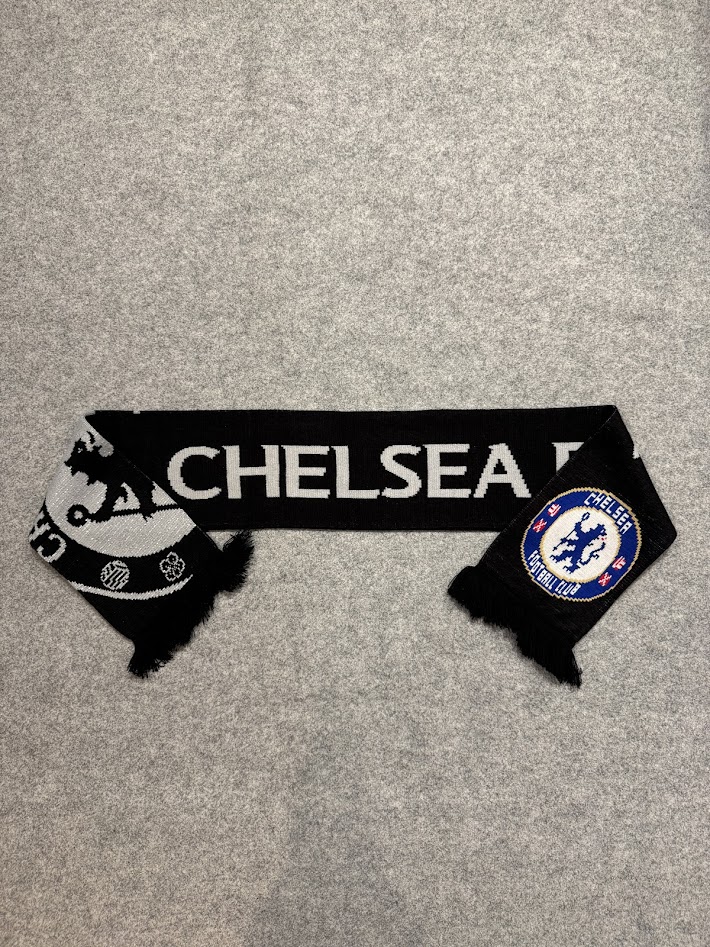 グレーの背景の上に平置きされたチェルシーFCサポーターマフラー。両端を折り返した状態。