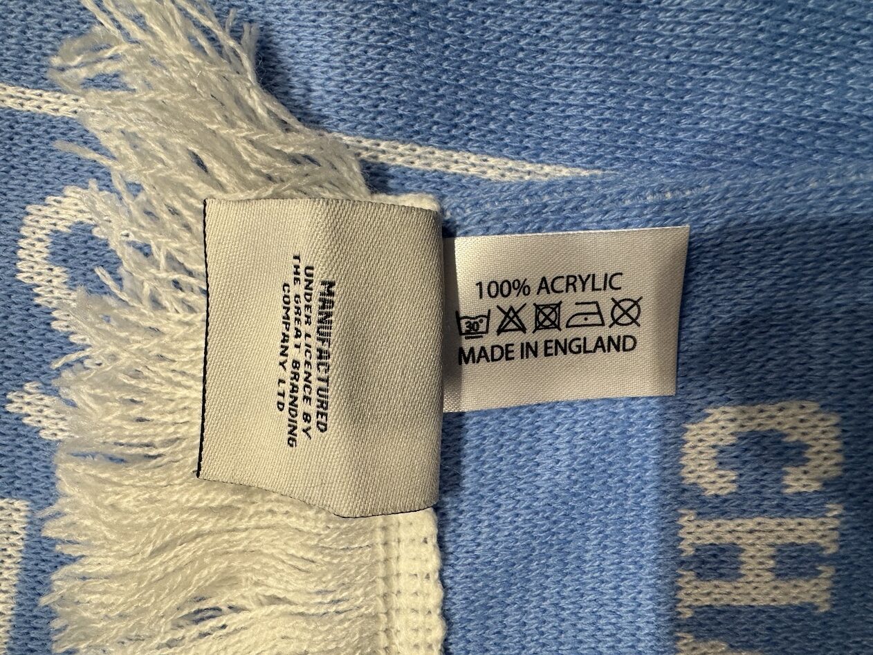 UEFA CHAMPIONS LEAGUE OFFICIAL LICENSED PRODUCT と表記されたタグ、MADE IN ENGLAND・100％ ACRYLIC と表記された品質表示タグのアップ。