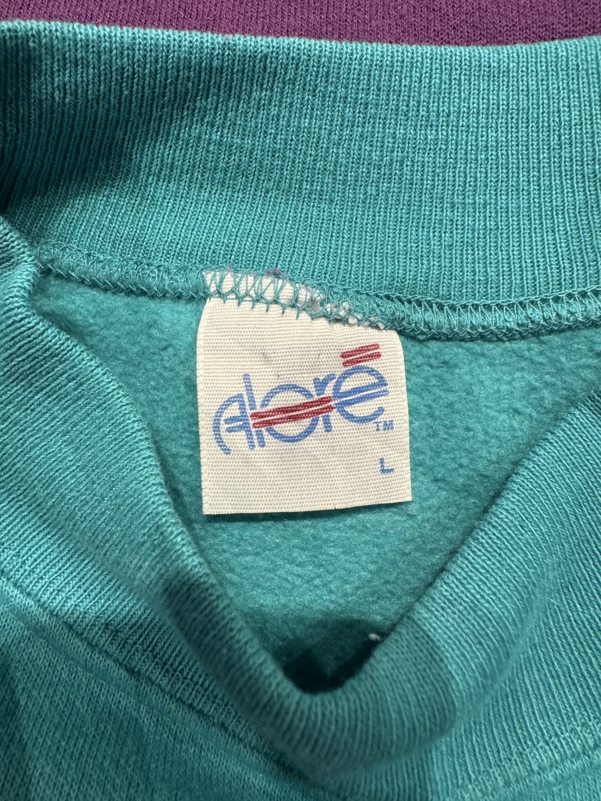 首元に付いたAloreロゴ入りブランドタグ。爽やかなターコイズカラーの裏起毛がのぞく。