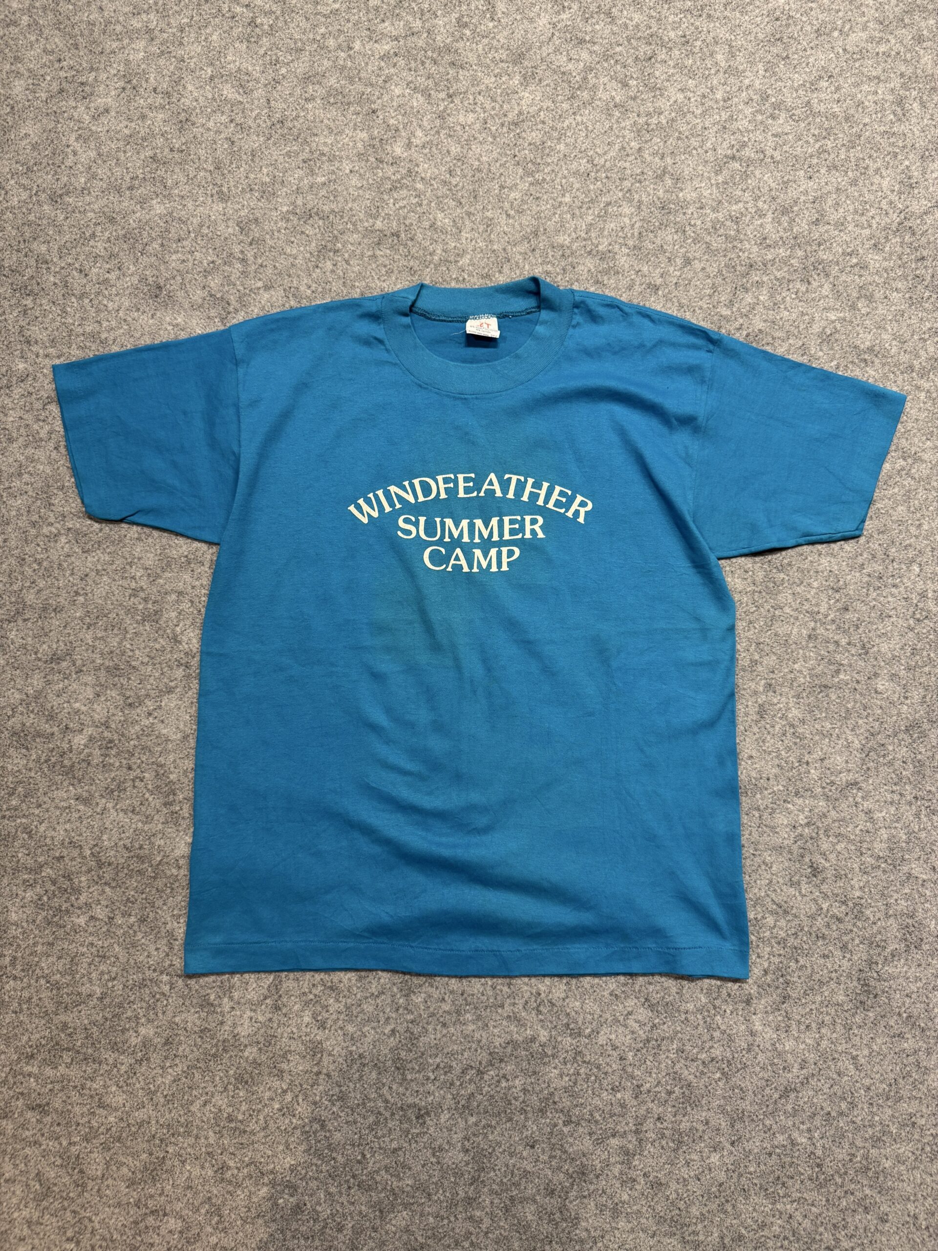 WINDFEATHER SUMMER CAMP Tシャツをグレーの床に平置きした全体写真(フロント)。