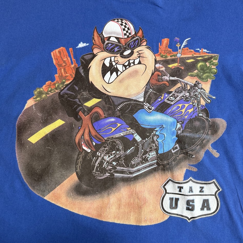 バイクに乗るタズとアメリカ西部の風景を描いた大型プリント