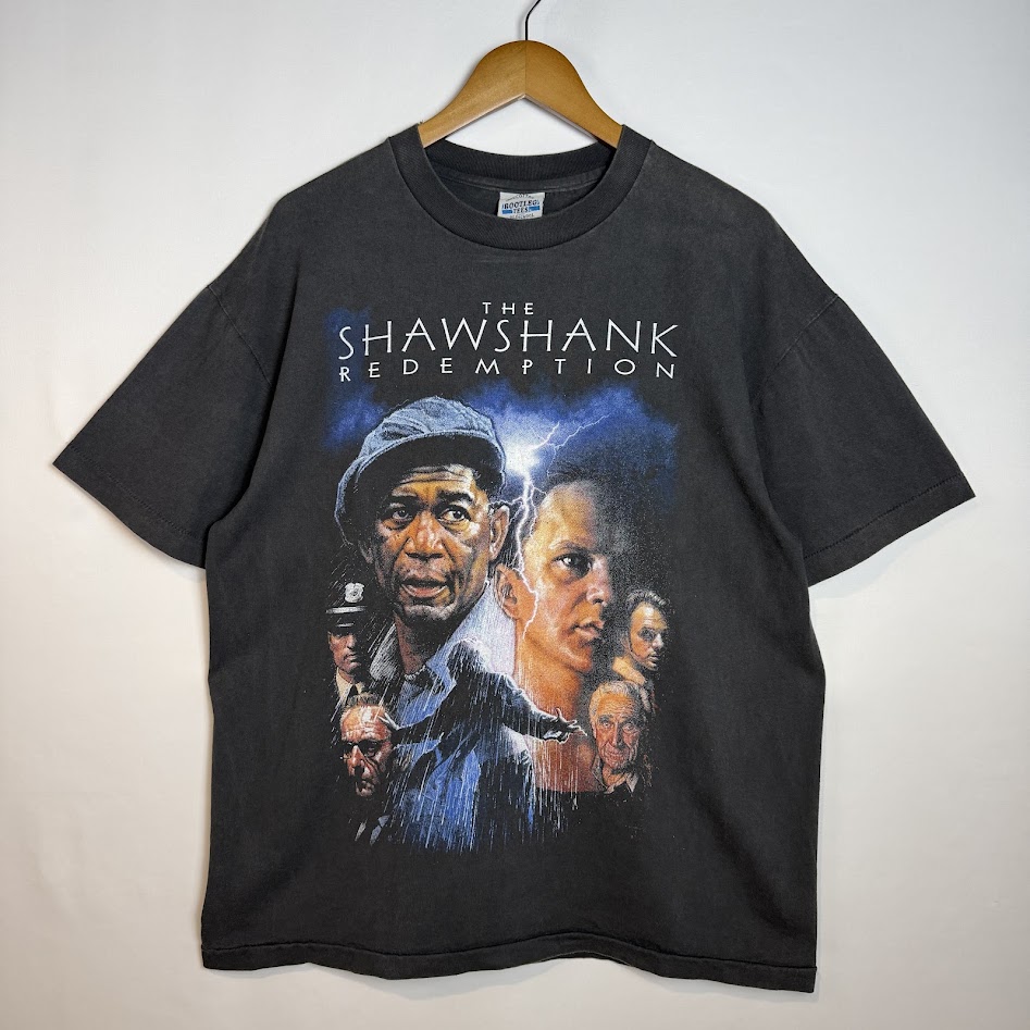『ショーシャンクの空に』の登場人物と雨の脱獄場面が描かれたブラックのムービーTシャツ前面