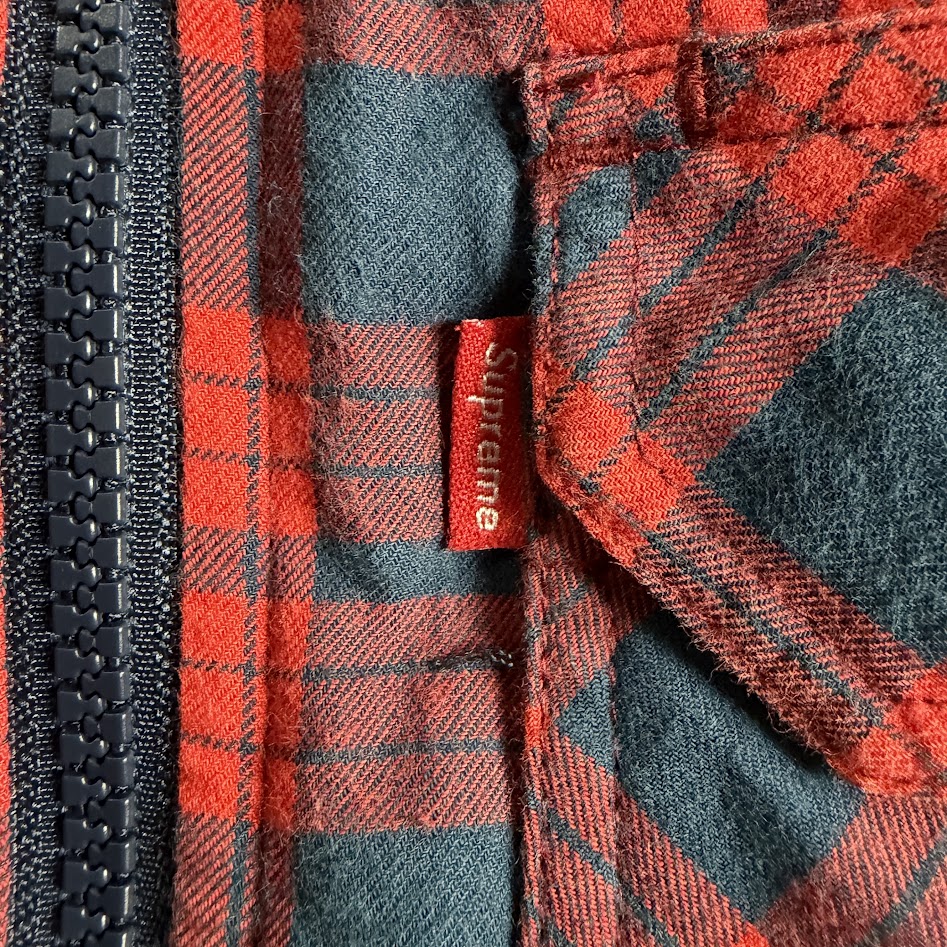 Supremeチェックジャケットの胸ポケットに付いた赤いブランドタグ
